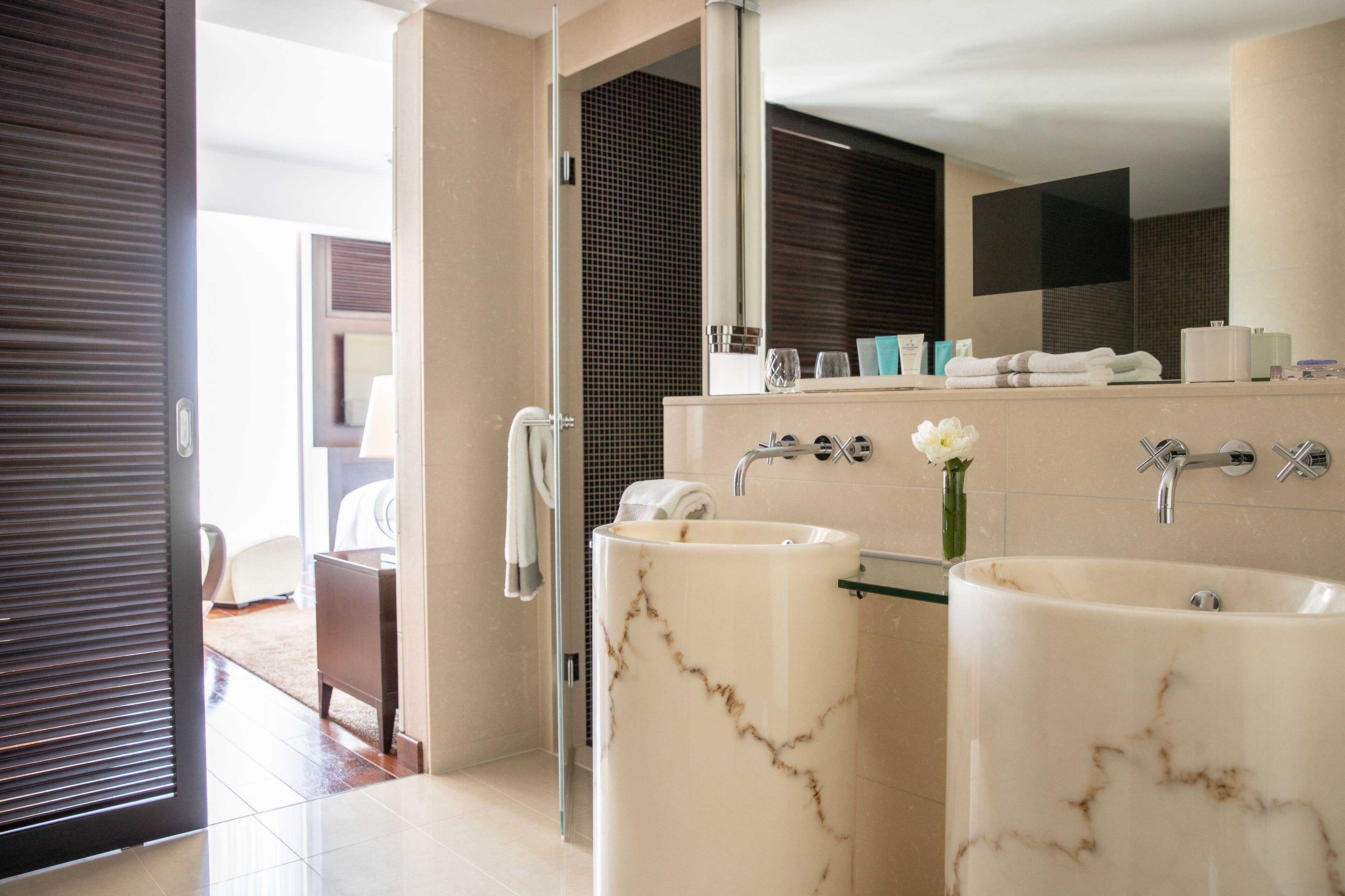 A modern bathroom with two large marble sinks, a glass shower enclosure, and a mirror above the sinks.