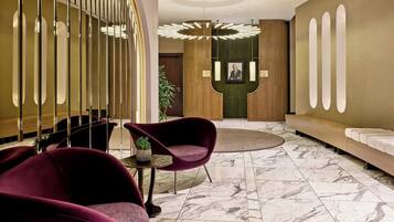 Eine moderne Lobby mit Marmorboden, einer Rezeption und einer Sitzecke mit violetten Stühlen.