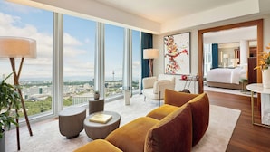 A modern hotel room with large windows, a sofa, a coffee table, and a bed.