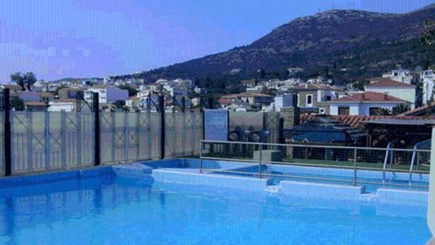 A swimming pool with a view of a mountainous landscape and residential buildings in the background. - Aeolis (Samos)