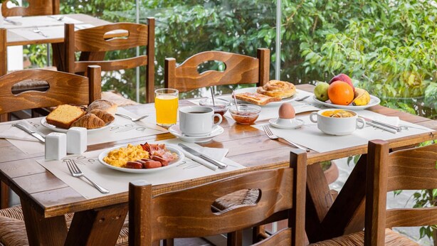 En frukostuppdukning med ett bord för två personer, med bland annat croissanter, rostat bröd, frukt och en skål med flingor.