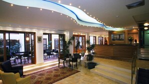En hotellobby med en receptionsdisk, en sittgrupp och stora fönster.