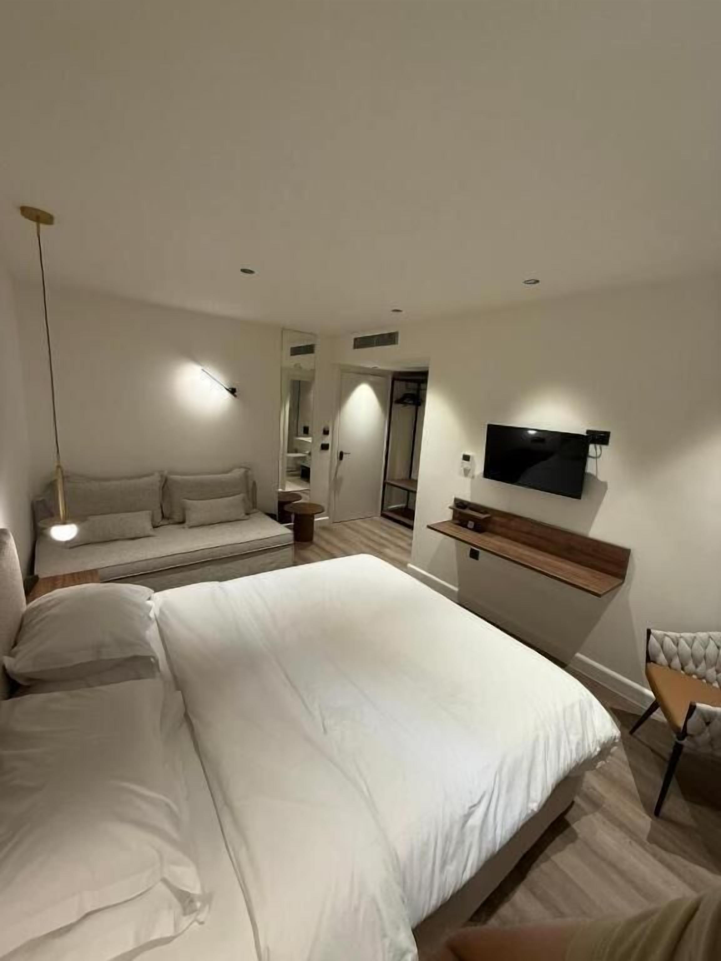 A modern bedroom with a large bed, a TV mounted on the wall, and a seating area with a chair and a small table.