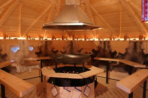 A wooden interior with a central fire pit, benches, and a large overhead vent. - Seehotel Luisenhof (Falkenhagen)