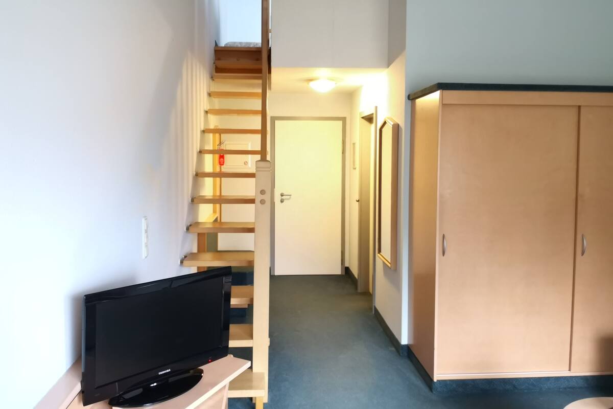 A hallway with a TV on a stand, a wooden staircase, and a door at the end.