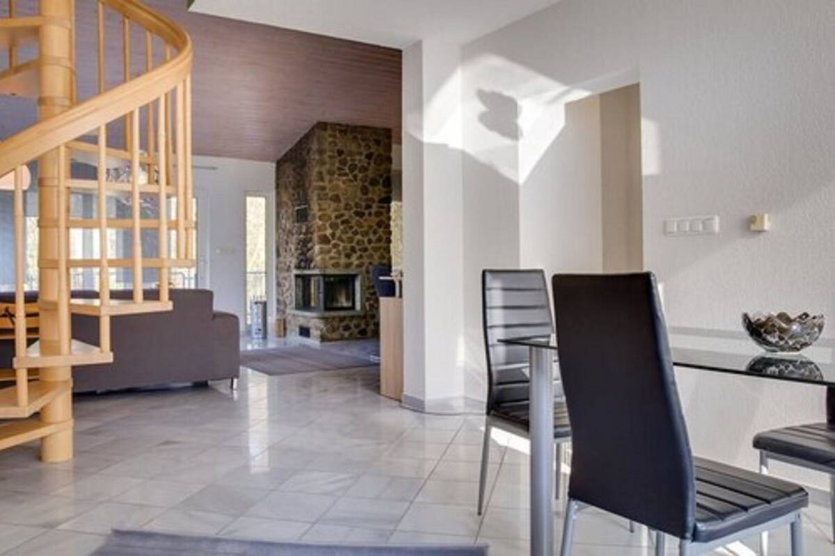 A modern interior with a spiral staircase, a stone fireplace, and a dining area with chairs and a glass table.