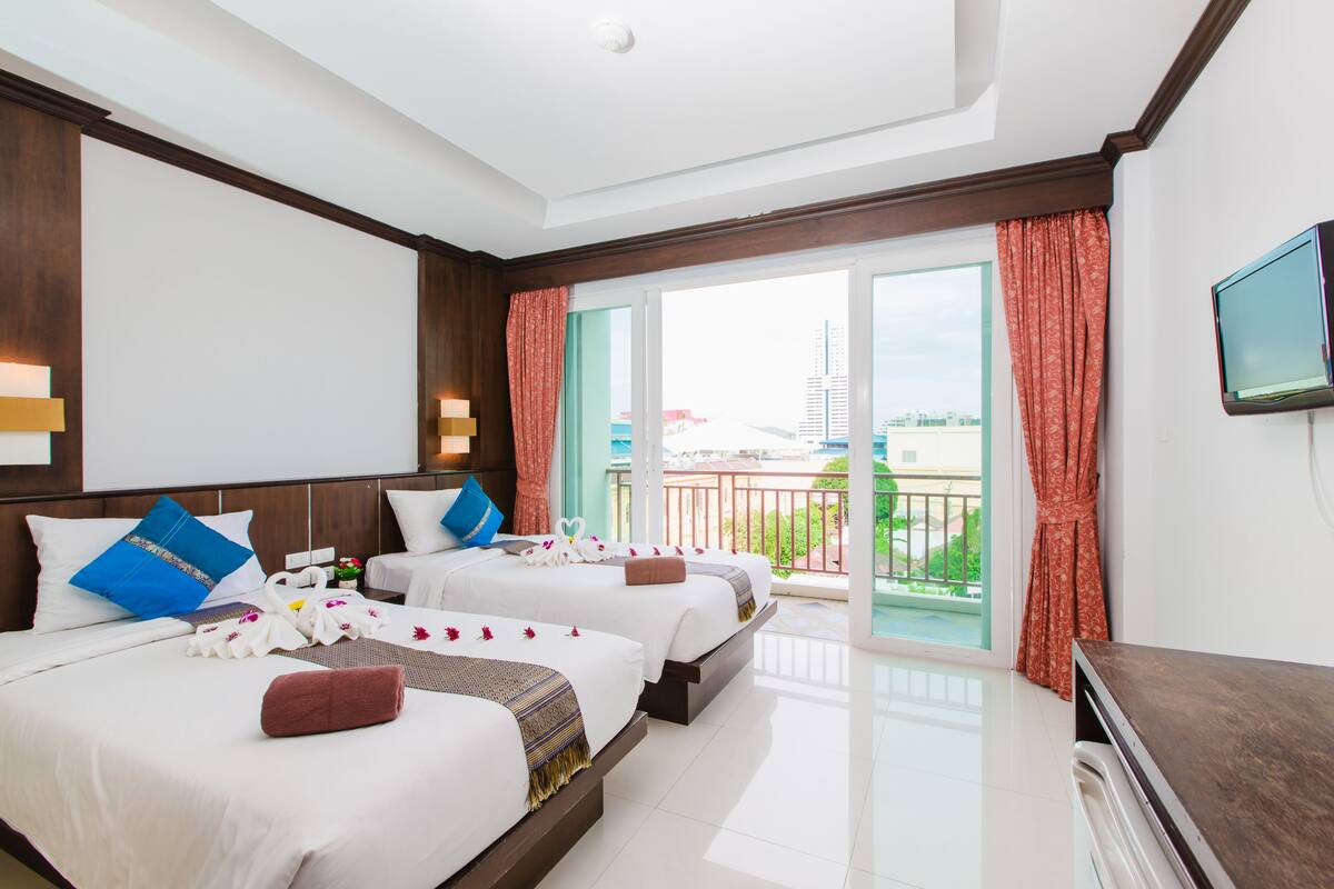 Habitación de hotel con dos camas, televisión y balcón con vistas.