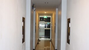 A corridor with a shiny tiled floor, a door with a number, and an emergency exit sign. - Azure Bangla Phuket (Patong)