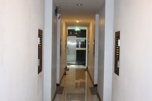 Un pasillo con piso de baldosas brillantes, una puerta numerada y un letrero de salida de emergencia.