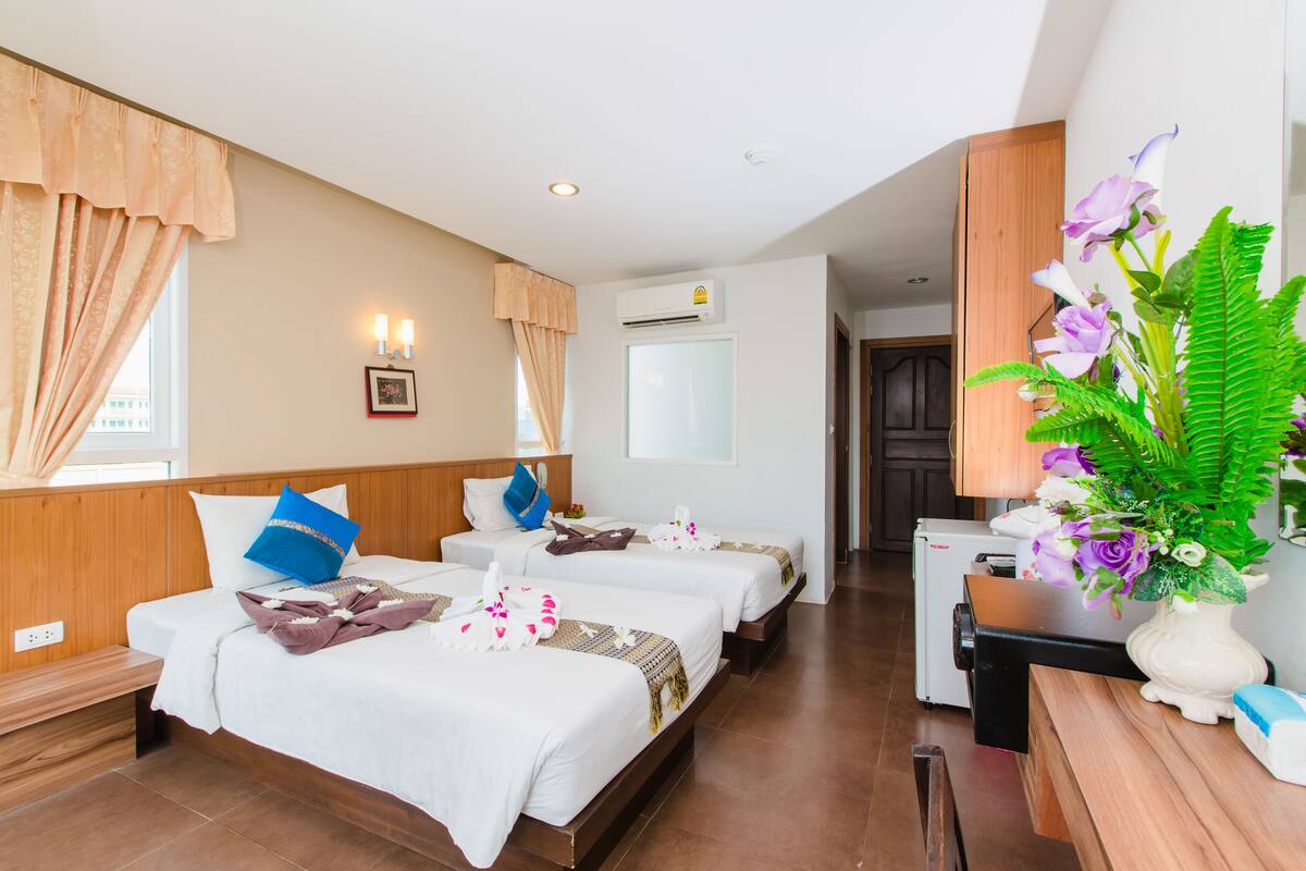 Habitación de hotel con dos camas, un escritorio, una silla, una mesita, una planta en maceta y un equipo de aire acondicionado.