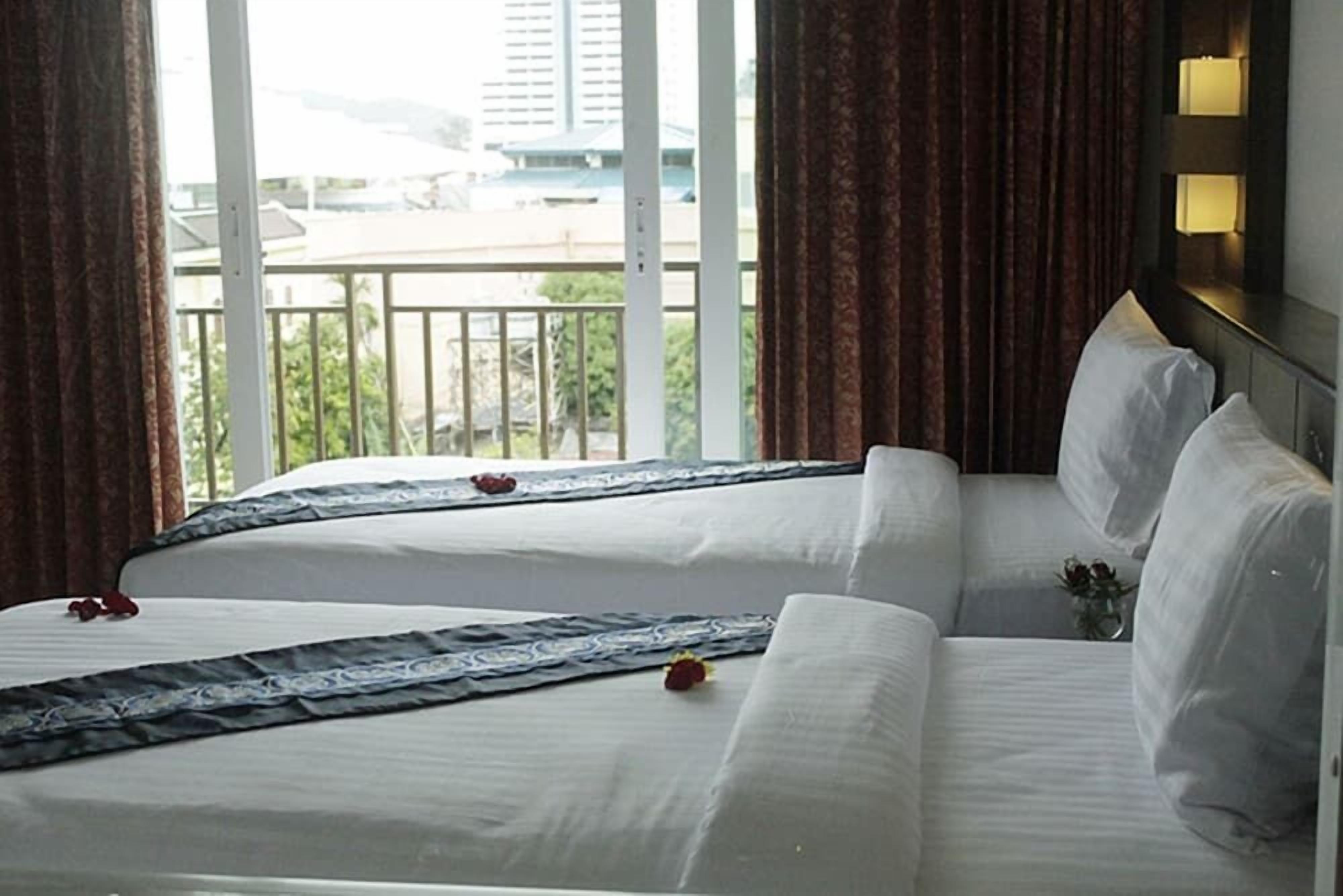 A hotel room with two beds, a balcony, and a view of buildings.