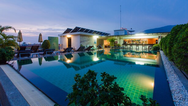 A swimming pool with lounge chairs and umbrellas, surrounded by greenery and a building with a modern design. - Azure Bangla Phuket (Patong)