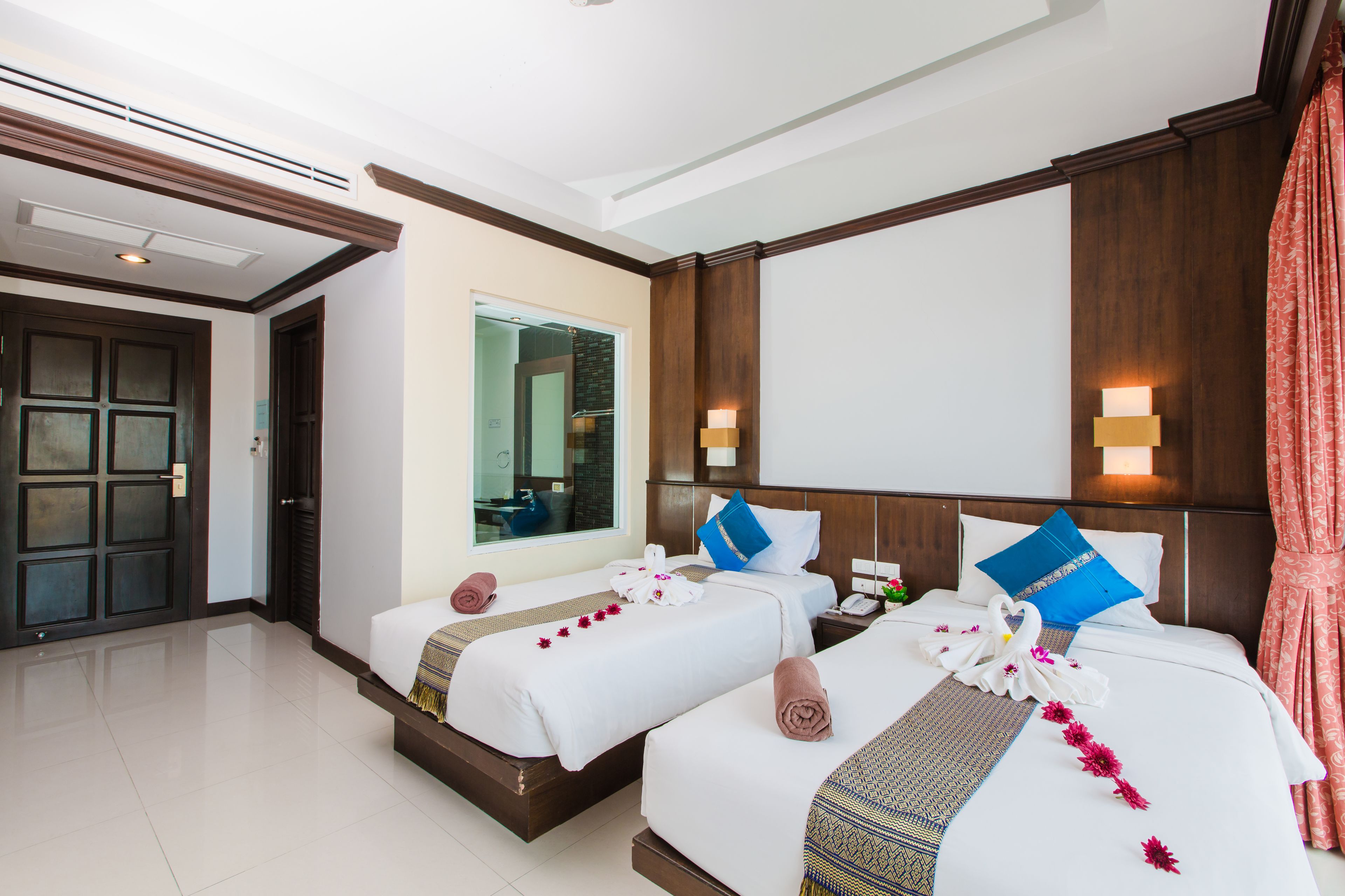 A hotel room with two beds, a large mirror, and a wooden headboard.