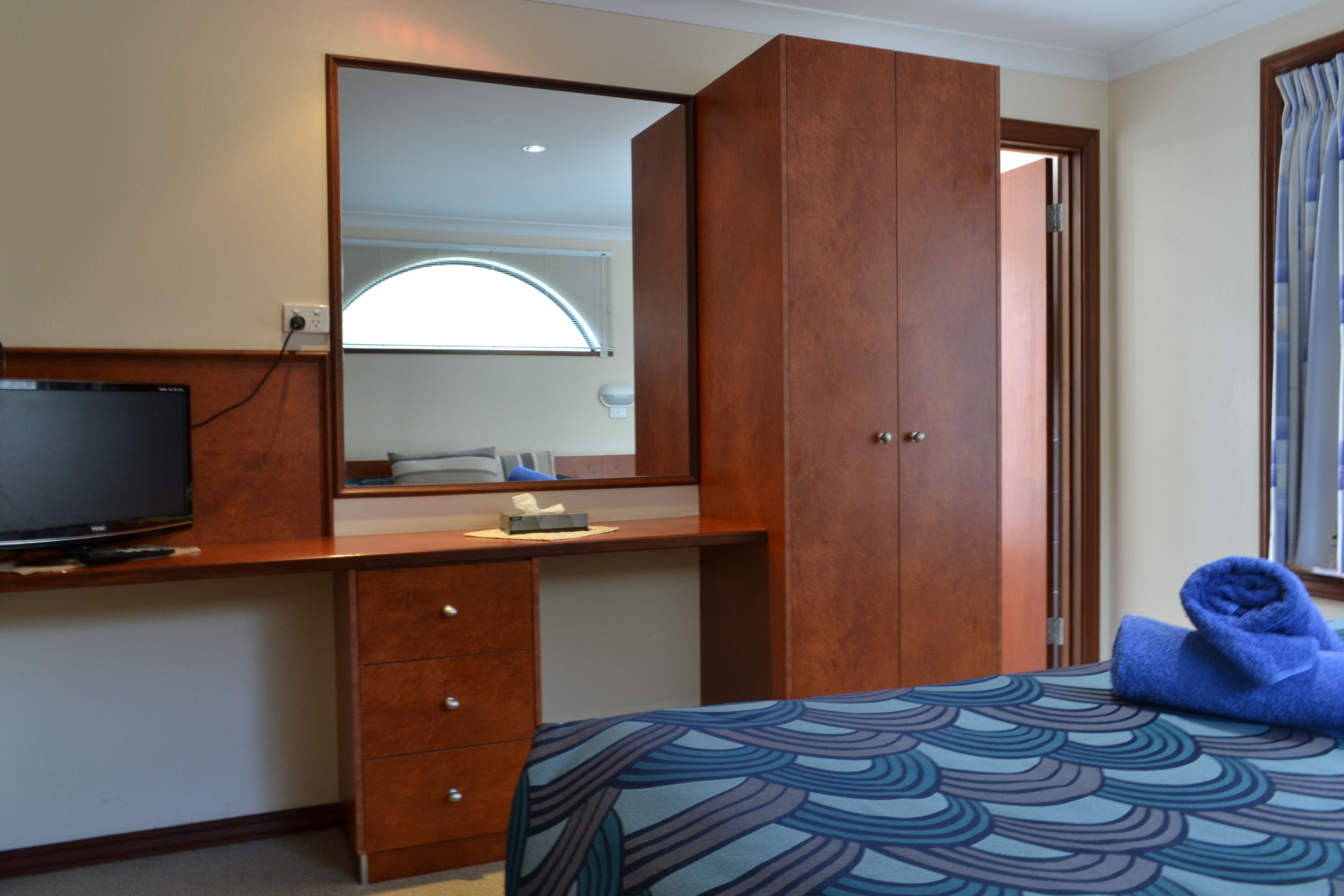 Una habitación de hotel con una cama, un escritorio con televisor, un espejo y una ventana con cortinas.