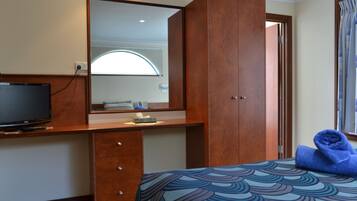 Una habitación de hotel con una cama, un escritorio con televisor, un espejo y una ventana con cortinas.
