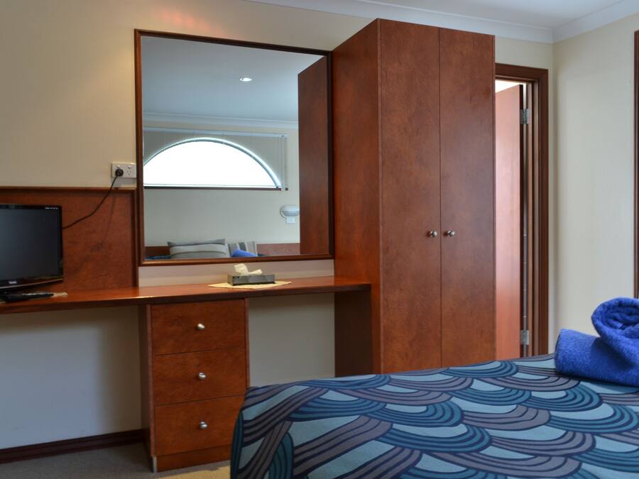 Una habitación de hotel con una cama, un escritorio con televisor, un espejo y una ventana con cortinas.