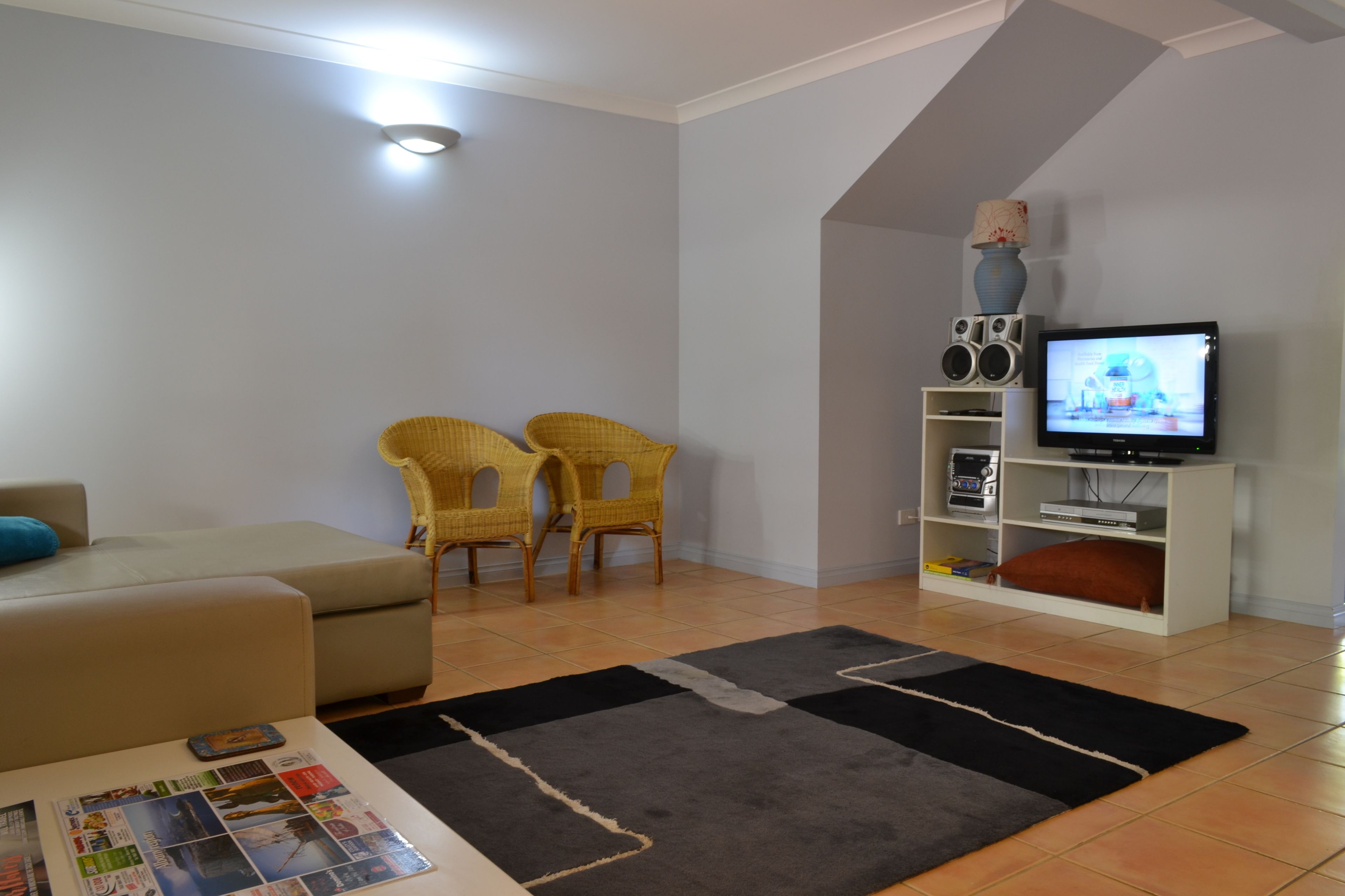 A living room with a sofa, two wicker chairs, a TV on a stand, and a bookshelf.