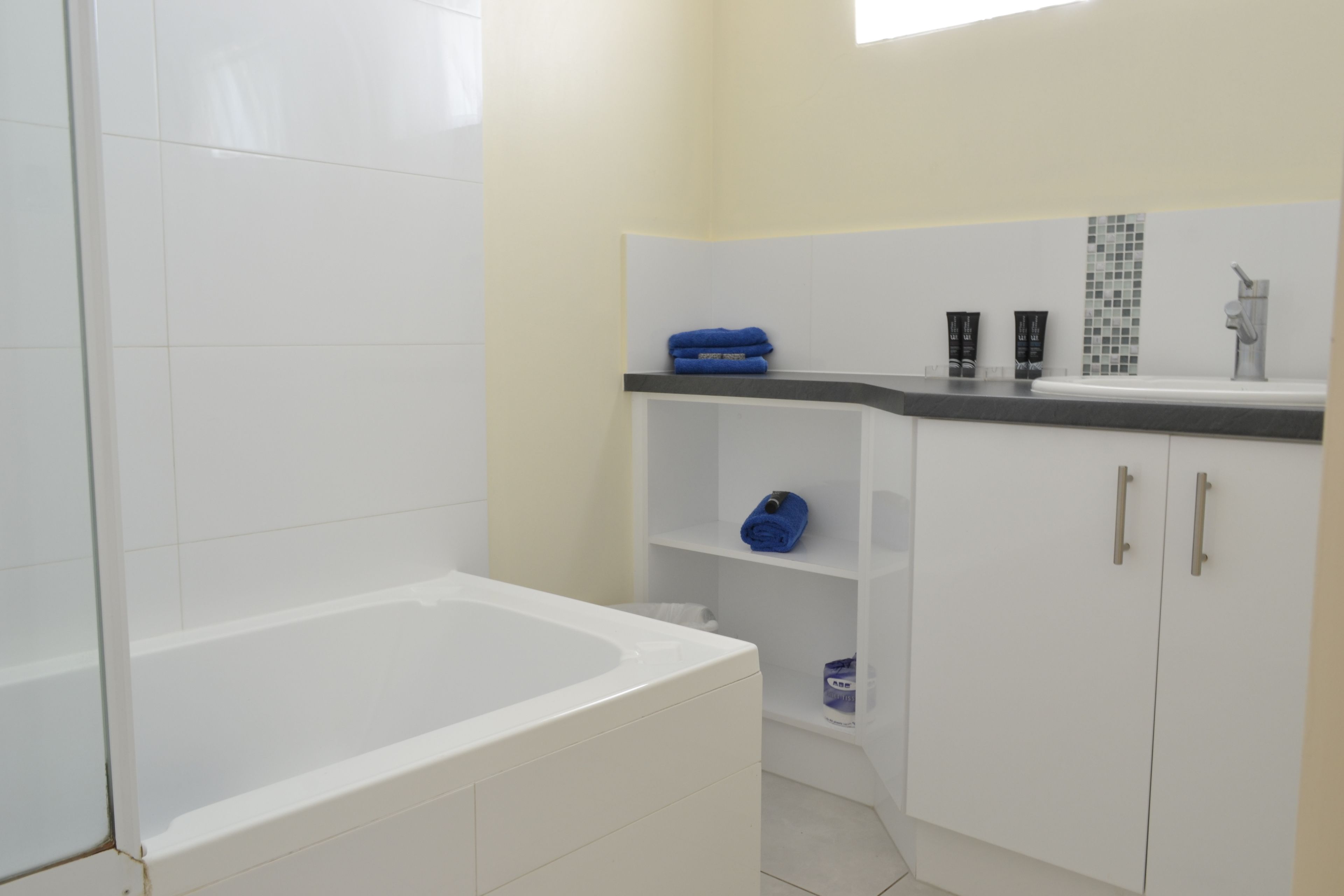 Une salle de bain avec une baignoire blanche, un lavabo avec un miroir et une étagère contenant des articles de toilette.
