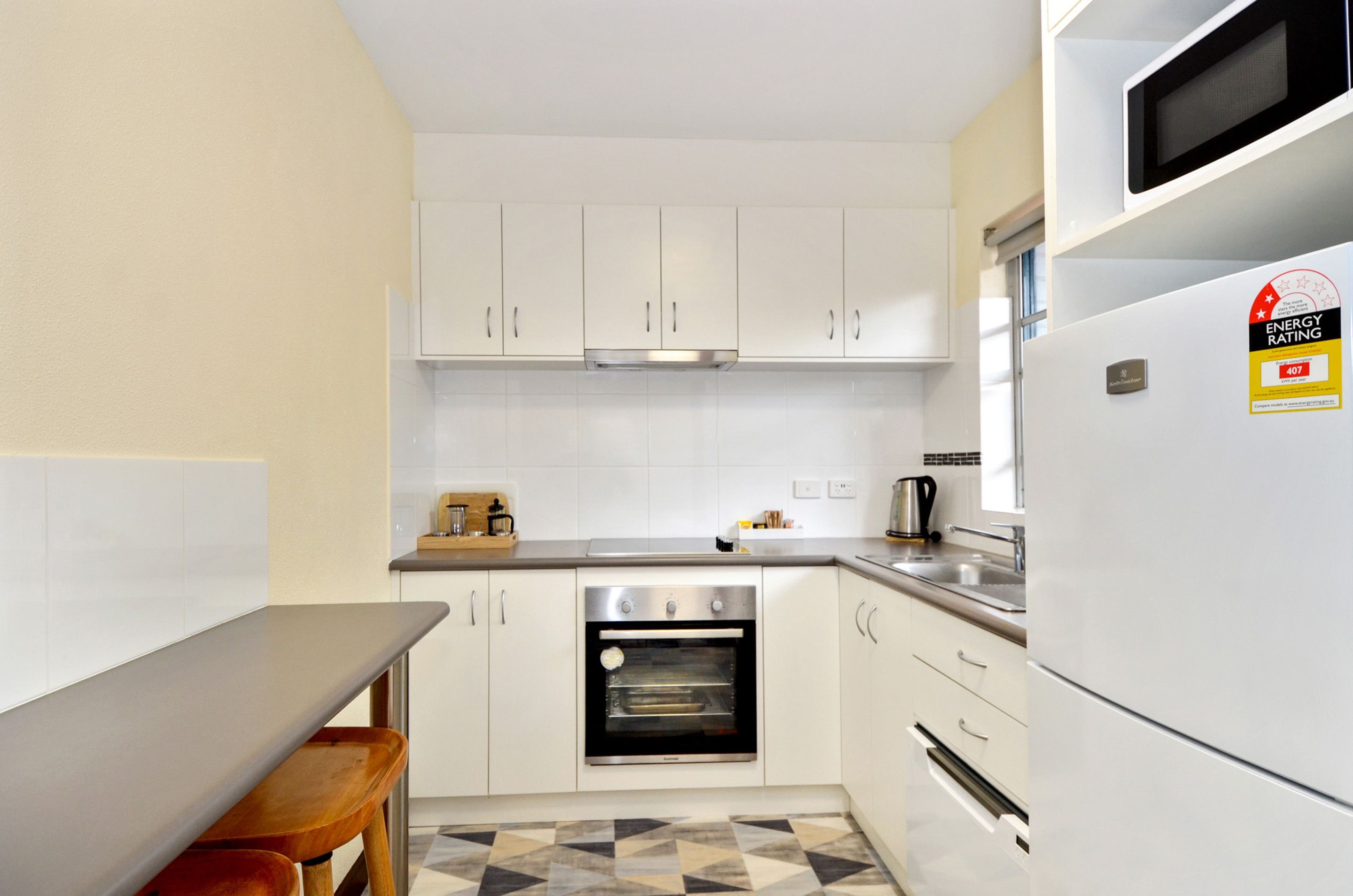 Una cocina compacta con armarios blancos, horno integrado, microondas y refrigerador.
