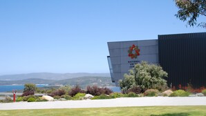 A building with a sign reading "National Australian Cancer Centre" and a view of the ocean and hills in the background. - Dolphin Lodge (Middleton Beach)