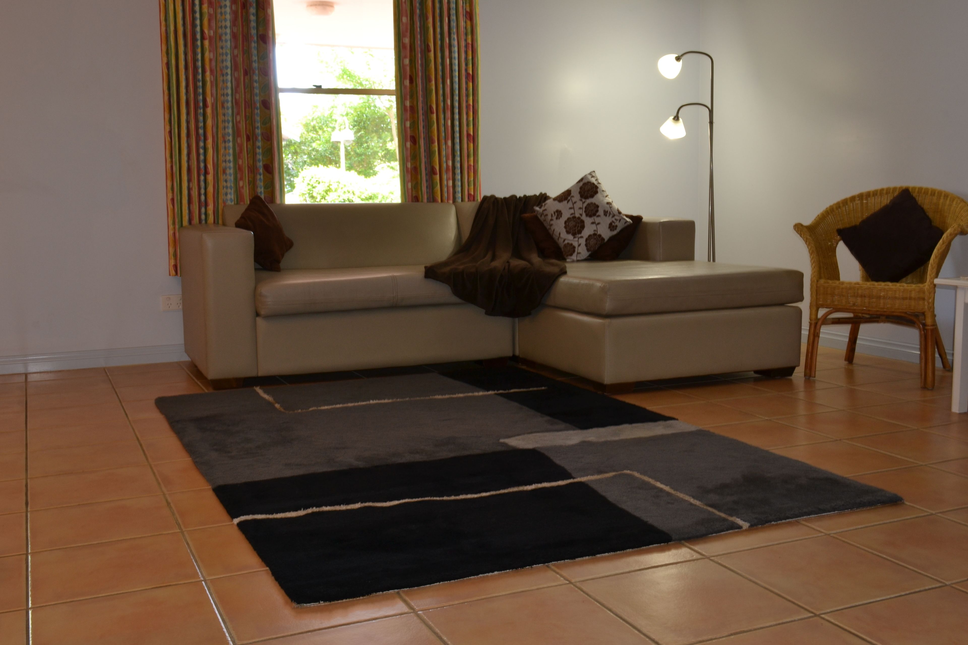 Un salon avec un canapé, un fauteuil, une lampe sur pied et une fenêtre avec des rideaux.