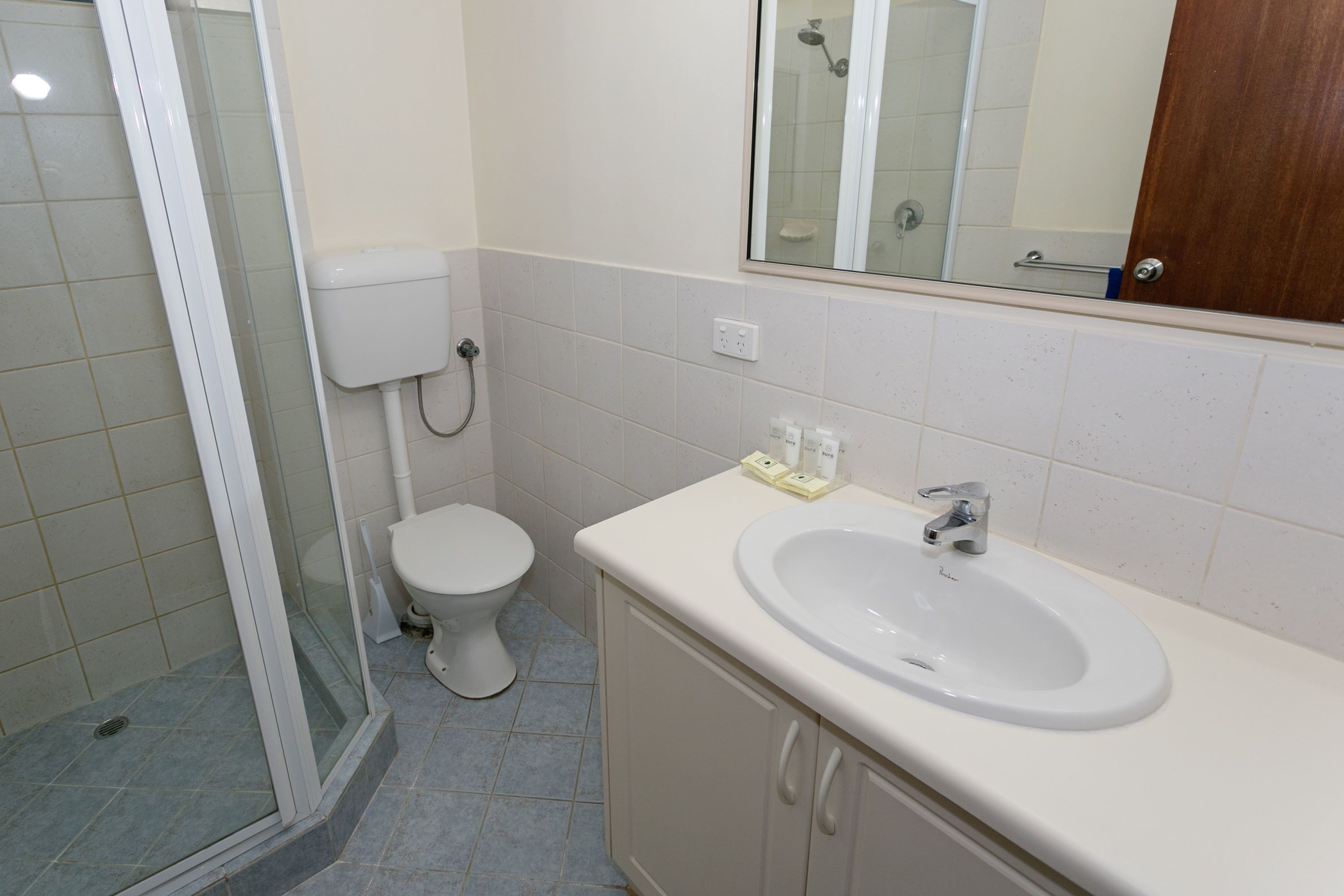 Een badkamer met douche, toilet, wastafel en spiegel.