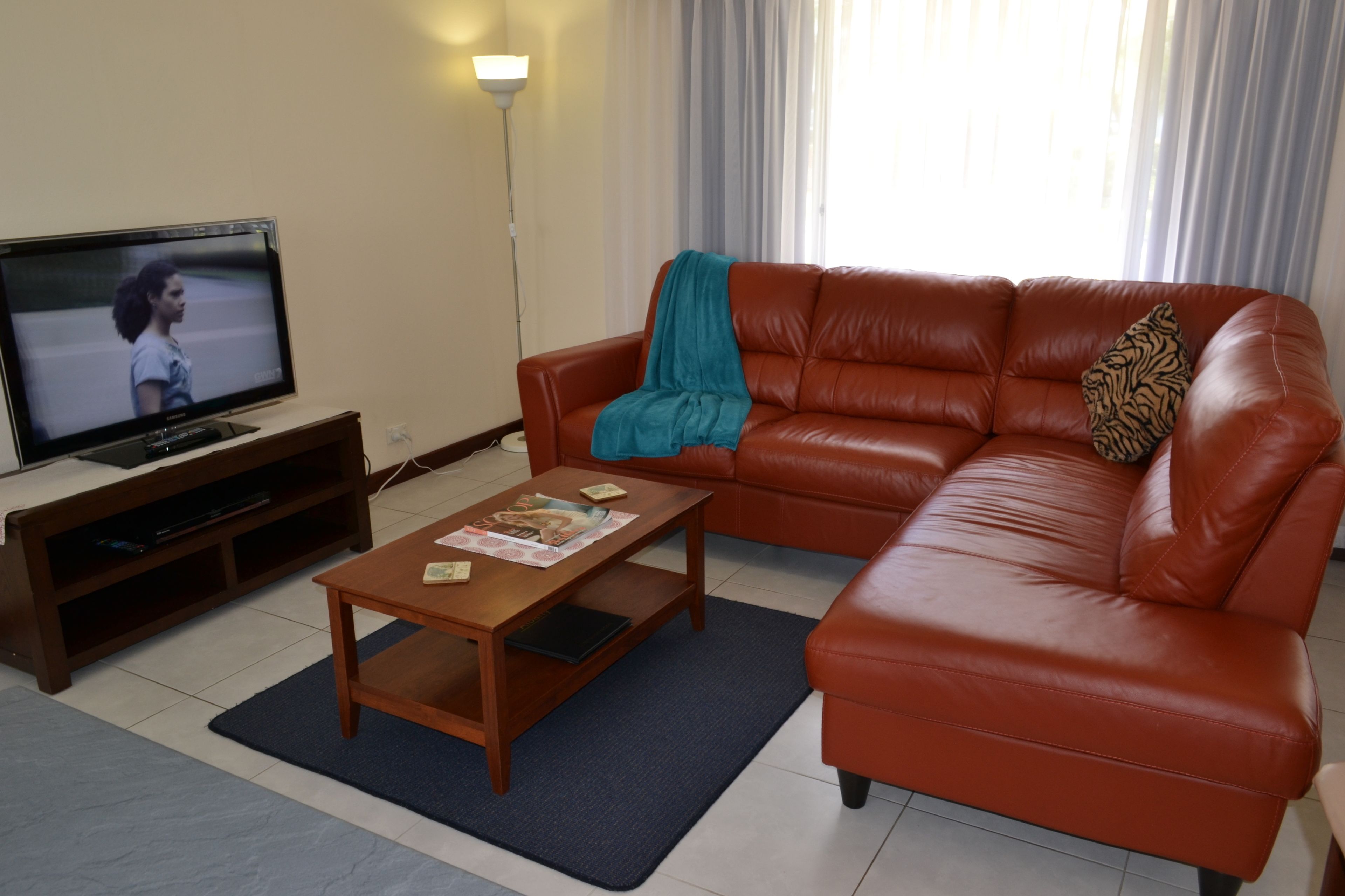 A living room with a brown leather sofa, a wooden coffee table, a television on a wooden stand, and a floor lamp.