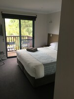A bedroom with a bed, a nightstand, a chair, and a view of a balcony with plants.