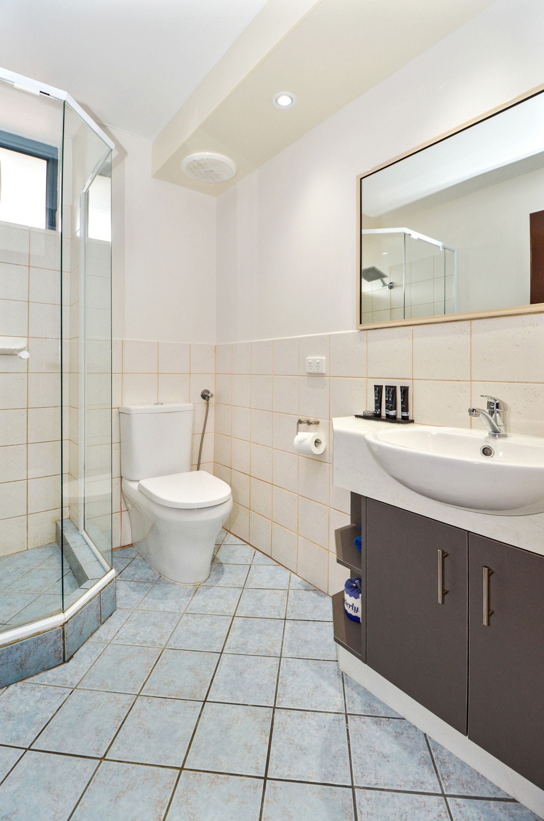 Een badkamer met een douchecabine van glas, een toilet, een wastafel met spiegel en betegelde vloer.