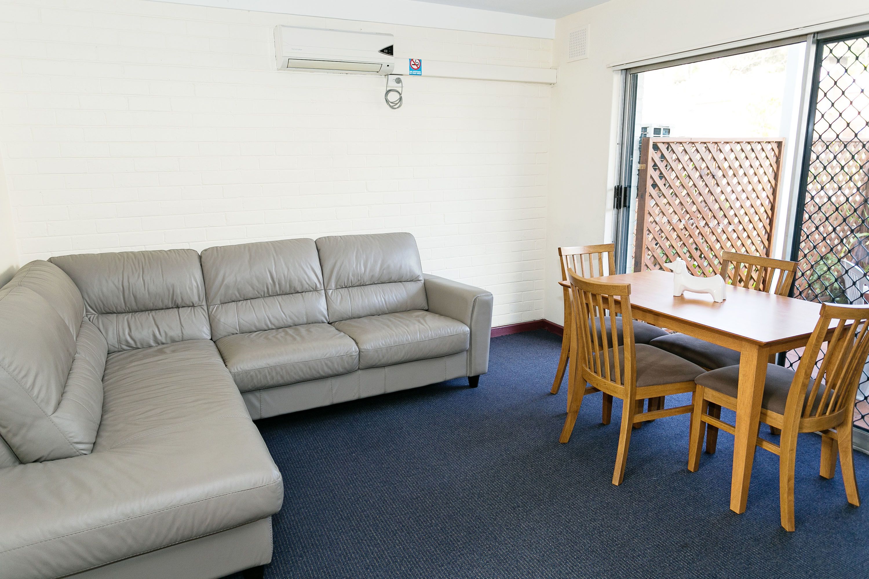 A room with a beige sectional sofa, a wooden dining table with four chairs, and a blue carpet.