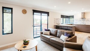 A modern living room with a sofa, a coffee table, and a kitchen area with a dining table and chairs. - Dolphin Lodge (Middleton Beach)