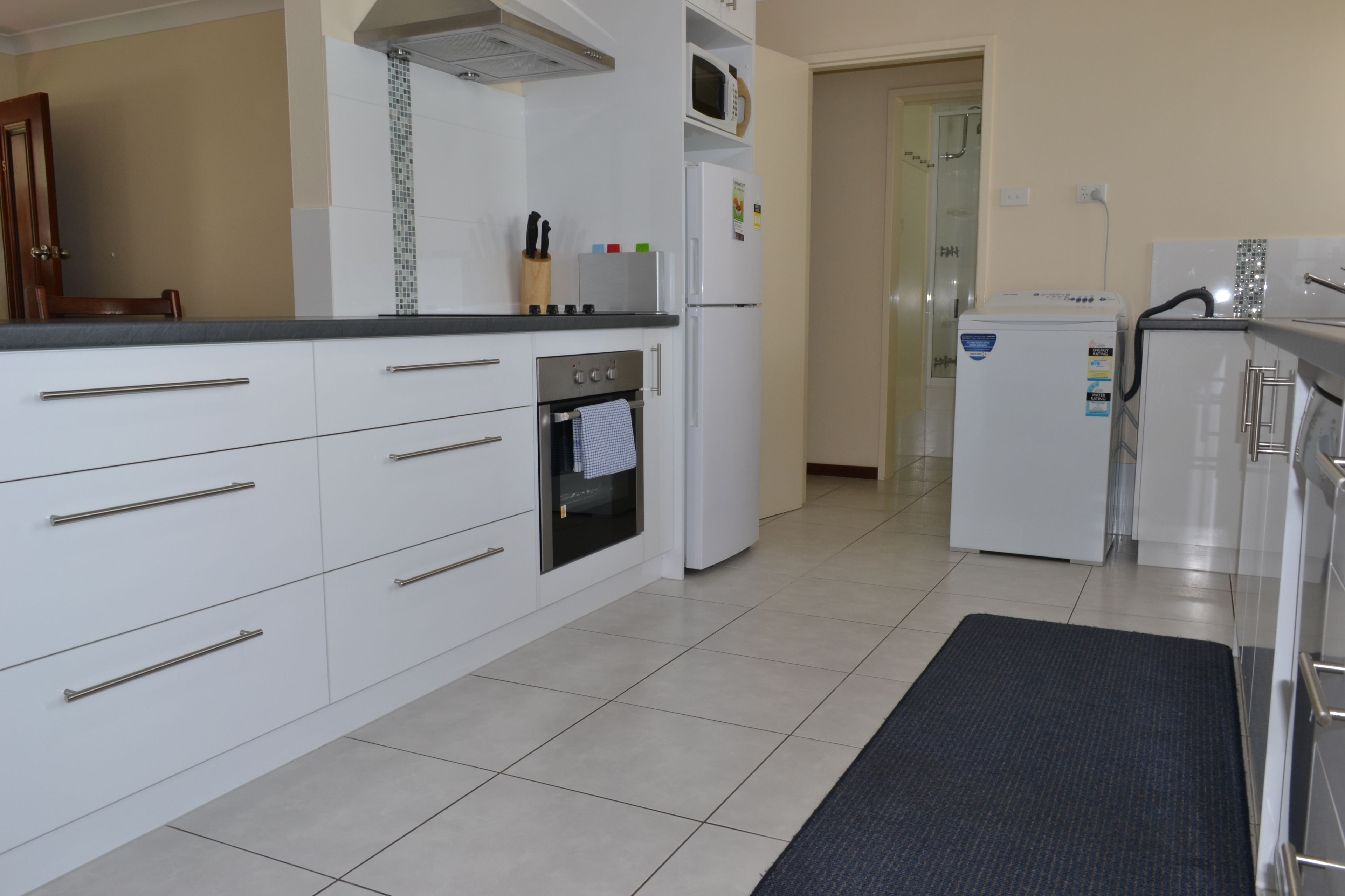 A modern kitchen with white cabinets, a built-in oven, a microwave, and a refrigerator.