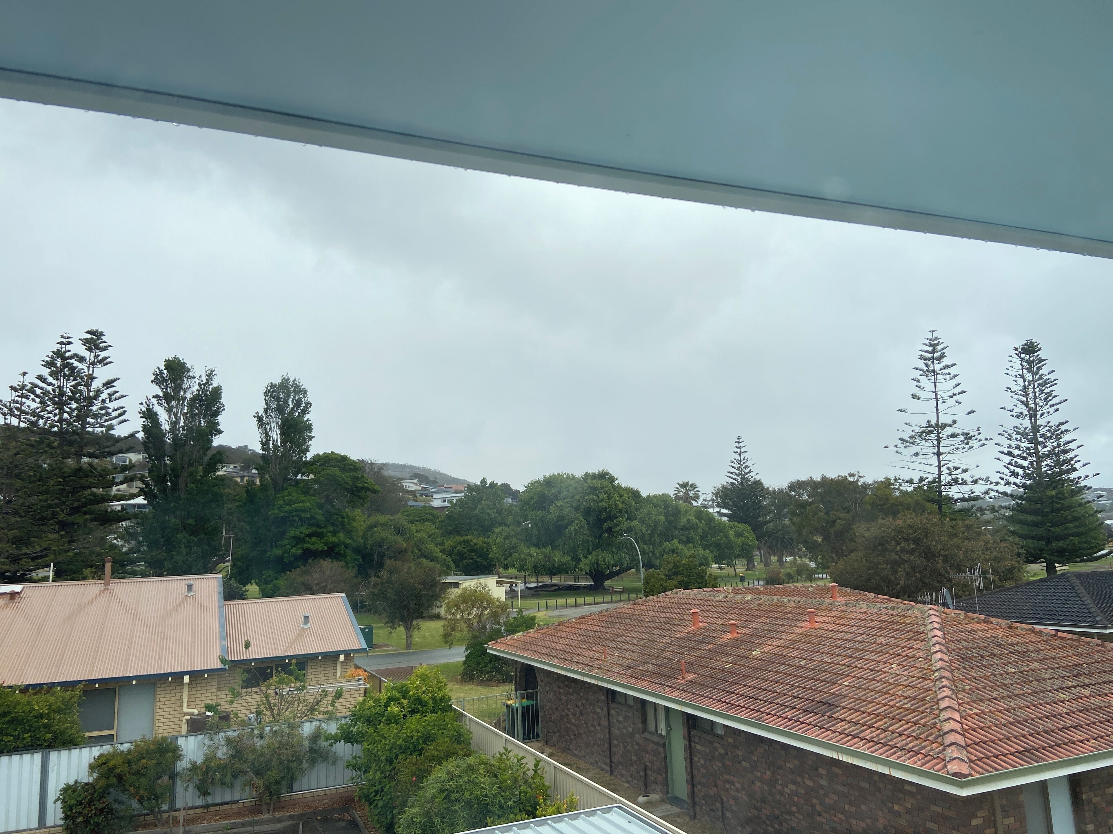 A residential area with houses, trees, and a hilly background.