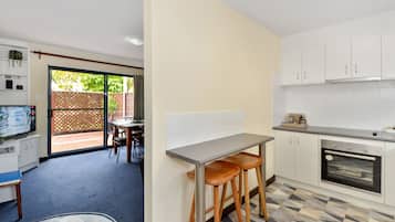 Une cuisine compacte dotée d’un four encastré, un coin repas avec une table et des chaises, et une vue sur l’extérieur grâce à une porte-fenêtre coulissante donnant sur un espace extérieur.