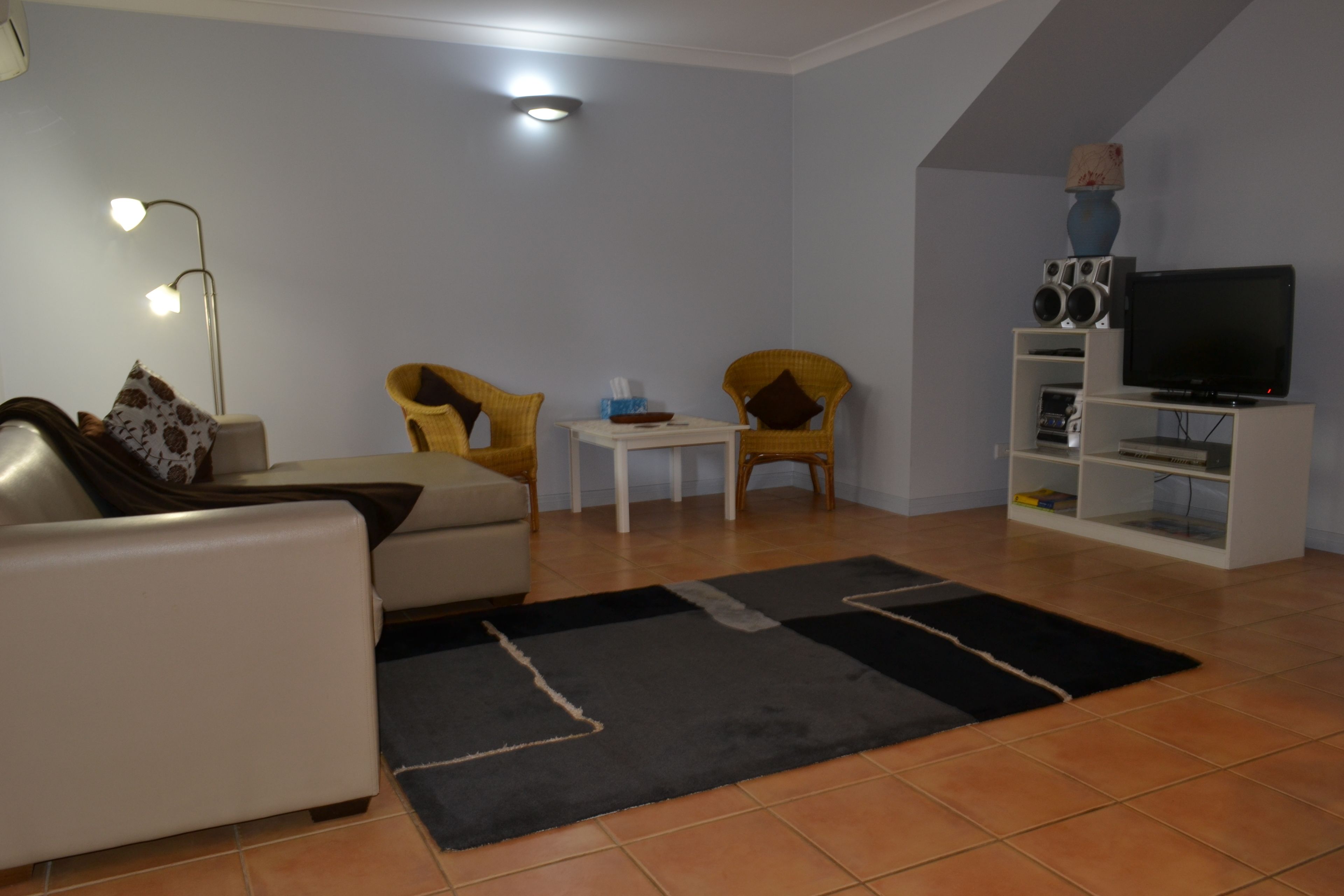 A living room with a sofa, two armchairs, a coffee table, a TV on a stand, and a bookshelf.