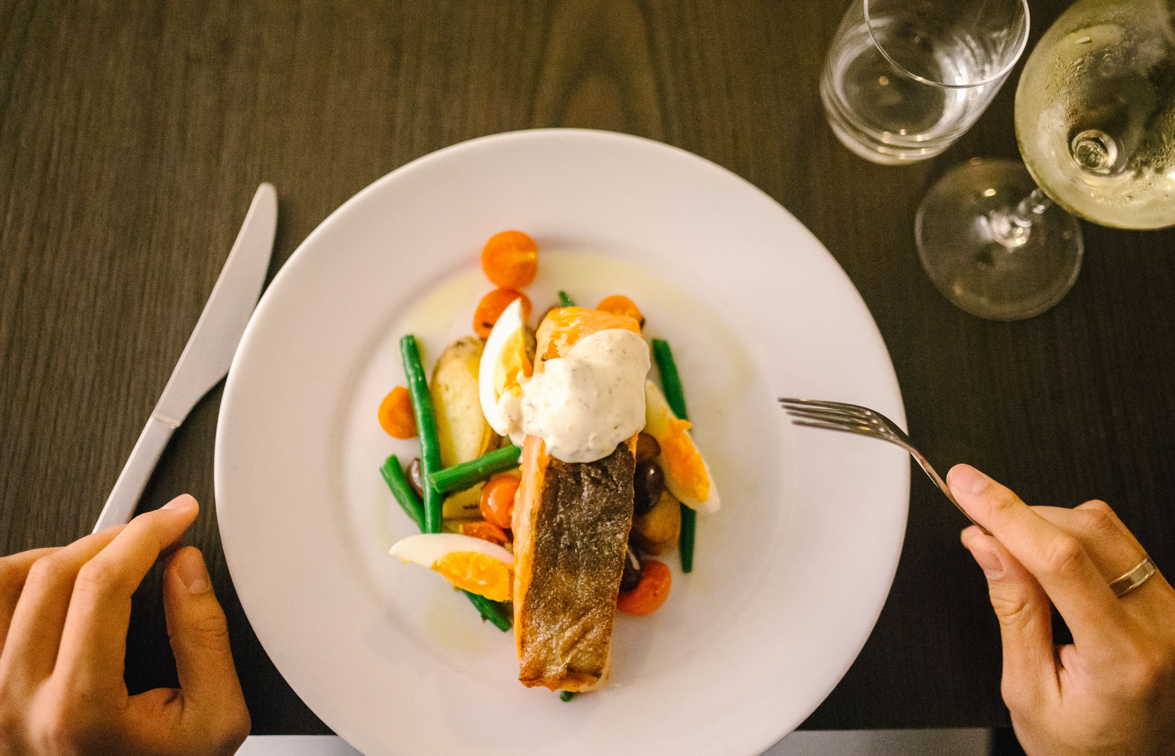 A plate of food with a fish, vegetables, and a dollop of sauce, accompanied by a fork and knife on a table.