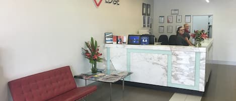 Una zona de recepción con mostrador de mármol, un banco rojo y diplomas enmarcados en la pared.