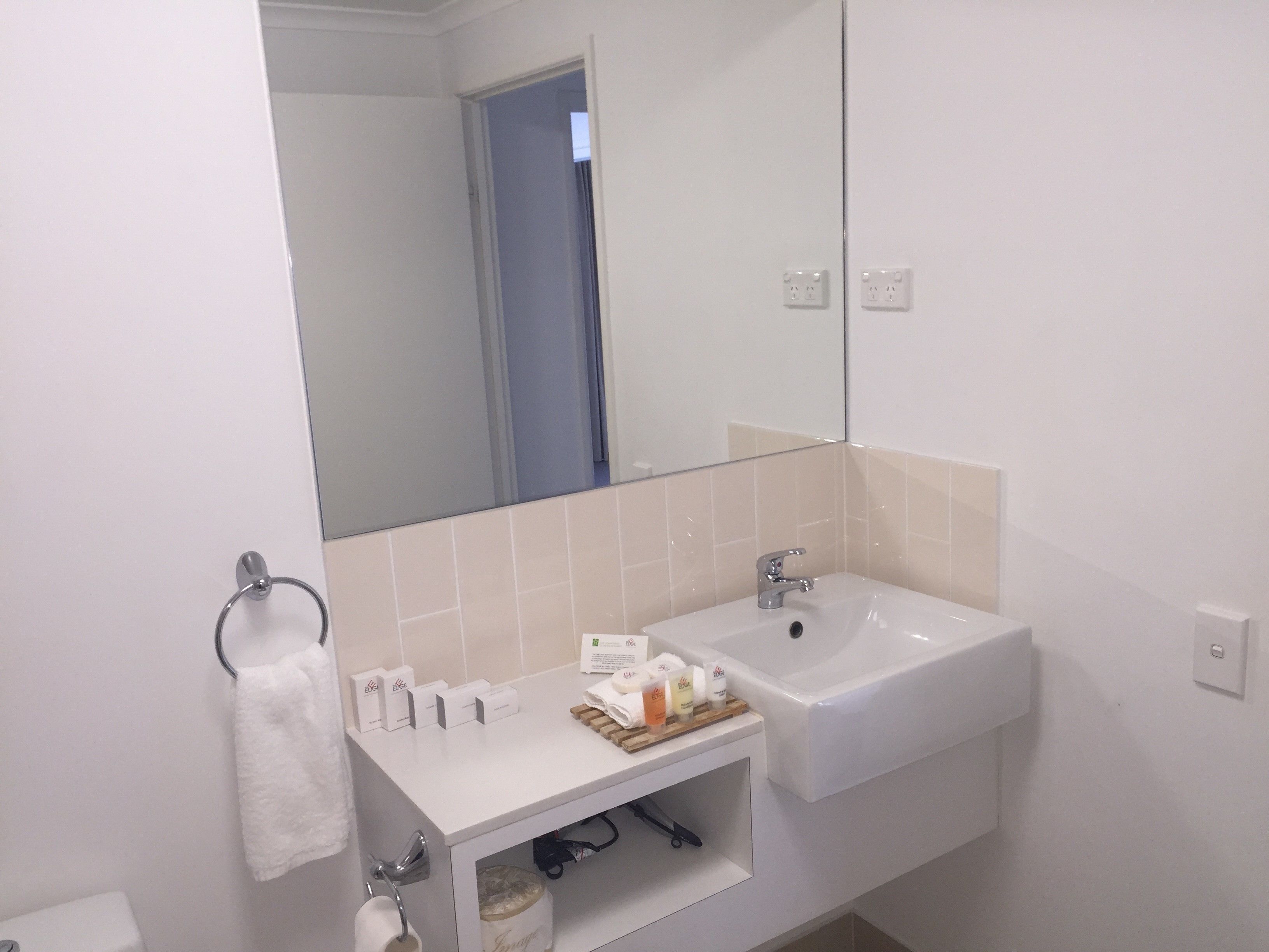 Een badkamer met een witte wastafel, spiegel en handdoekhouder.
