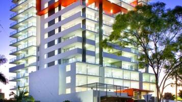 Un hotel moderno de varios pisos con una fachada distintiva en rojo y blanco, grandes ventanales y una zona de entrada bien iluminada.