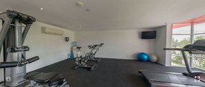 Un gimnasio con equipamiento de ejercicio, una cinta de correr y un ventanal con vistas a zonas verdes.