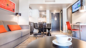 A modern hotel room with a sofa, a dining table with chairs, a kitchen area, and a TV on the wall. - Aparthotel Adagio Marseille Timone (Marseille)