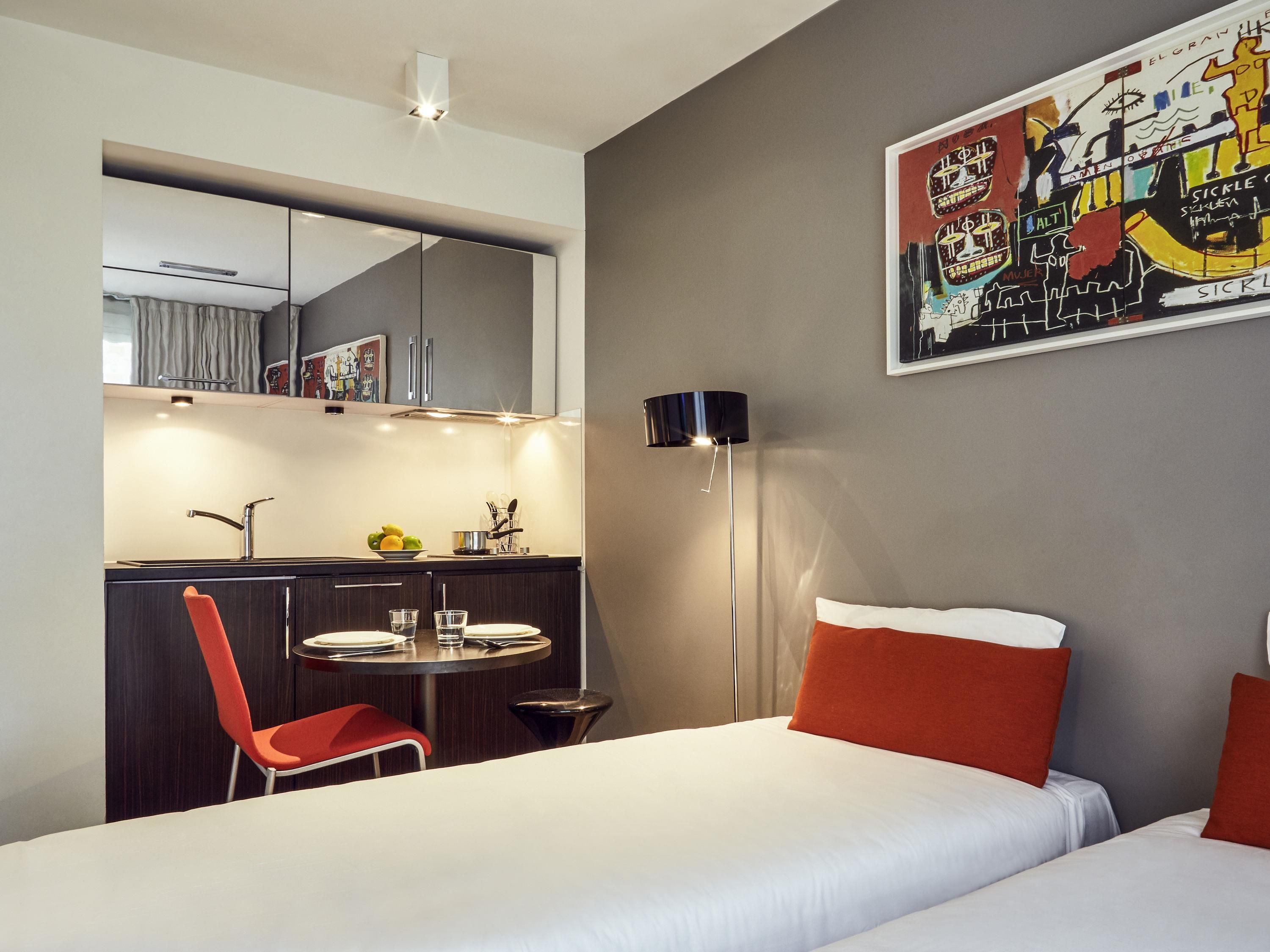 Une chambre d’hôtel moderne équipée d’un lit, d’un bureau avec une chaise, d’une table ronde et d’un grand miroir.