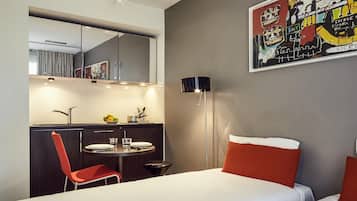 Une chambre d’hôtel moderne équipée d’un lit, d’un bureau avec une chaise, d’une table ronde et d’un grand miroir.