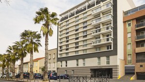 A multi-story hotel with balconies, palm trees, and parked cars. - Aparthotel Adagio Marseille Timone (Marseille)