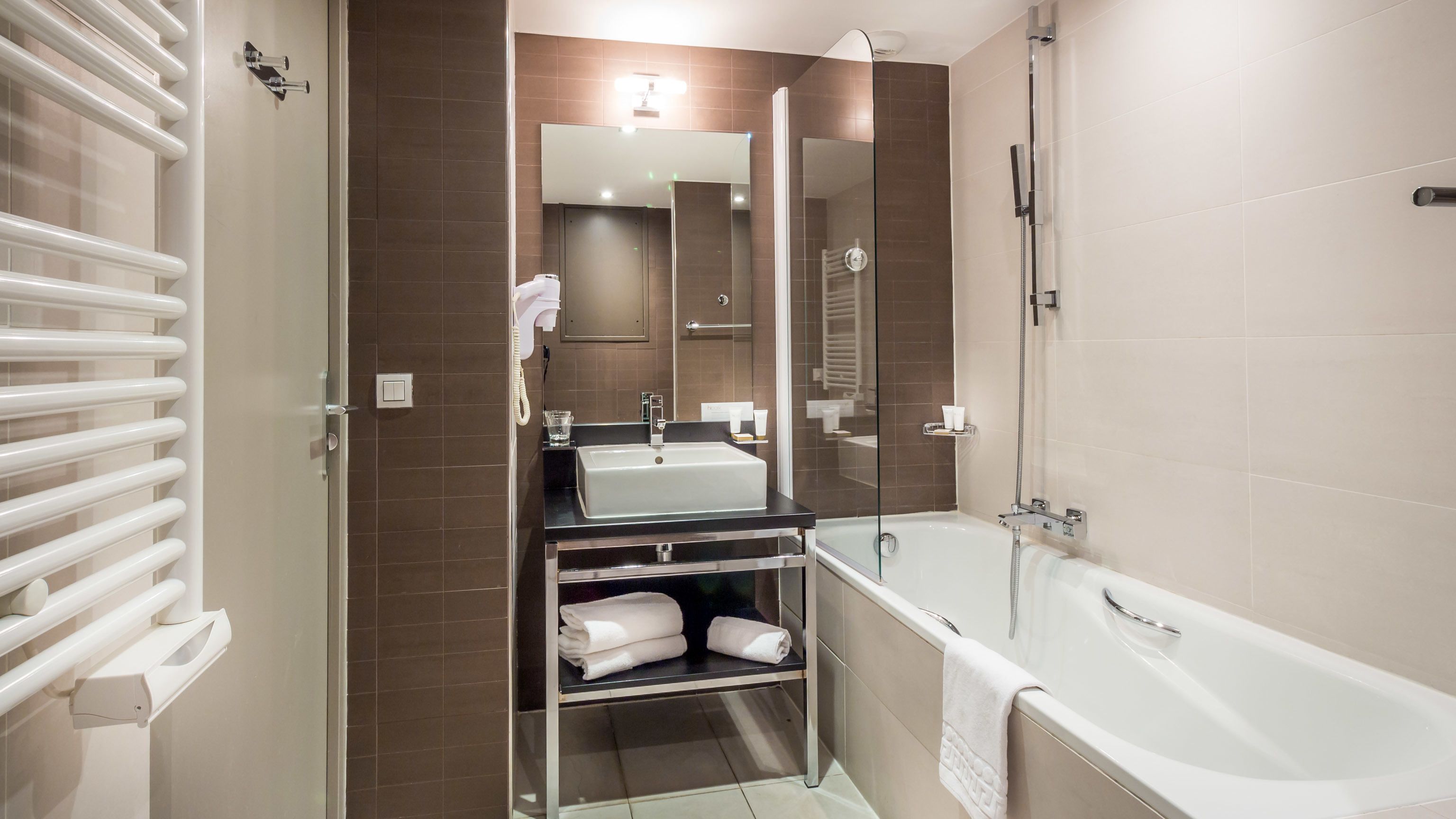 A modern bathroom with a glass-enclosed shower, a white bathtub, and a vanity with a sink and towel rack.