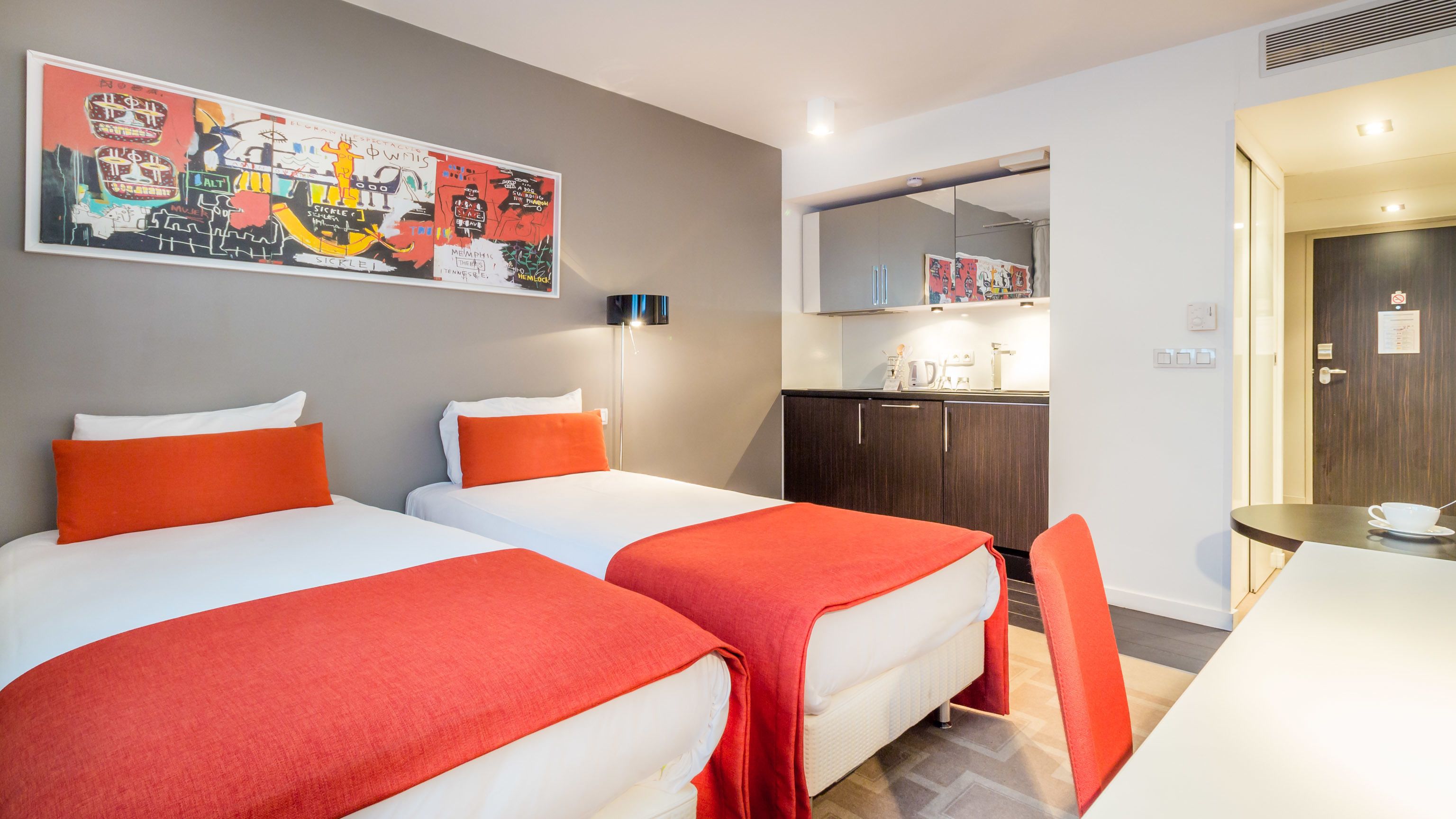 A hotel room with two beds, a kitchenette, and a dining area.