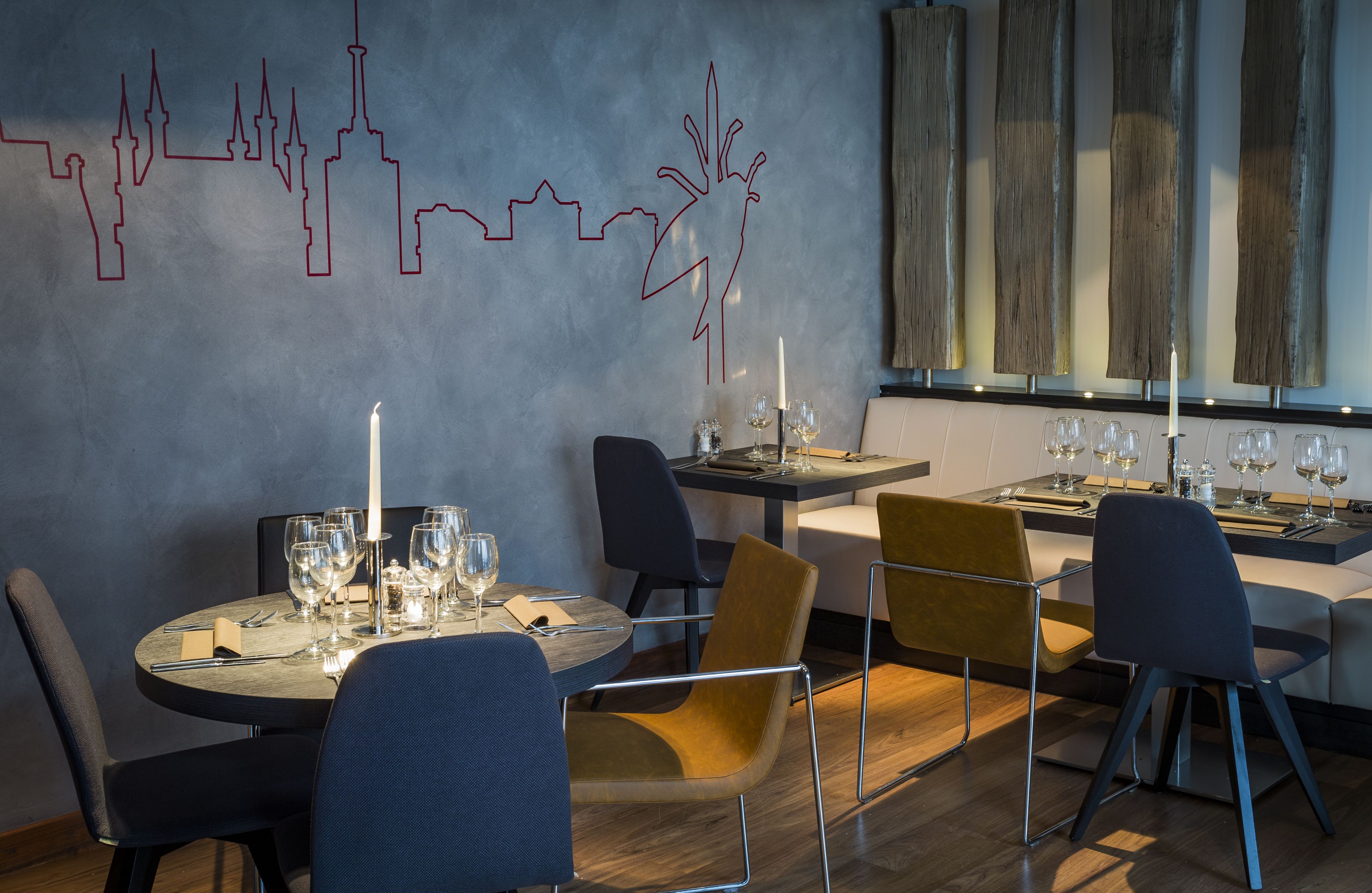A modern dining area with round tables, chairs, and a cityscape mural on the wall.