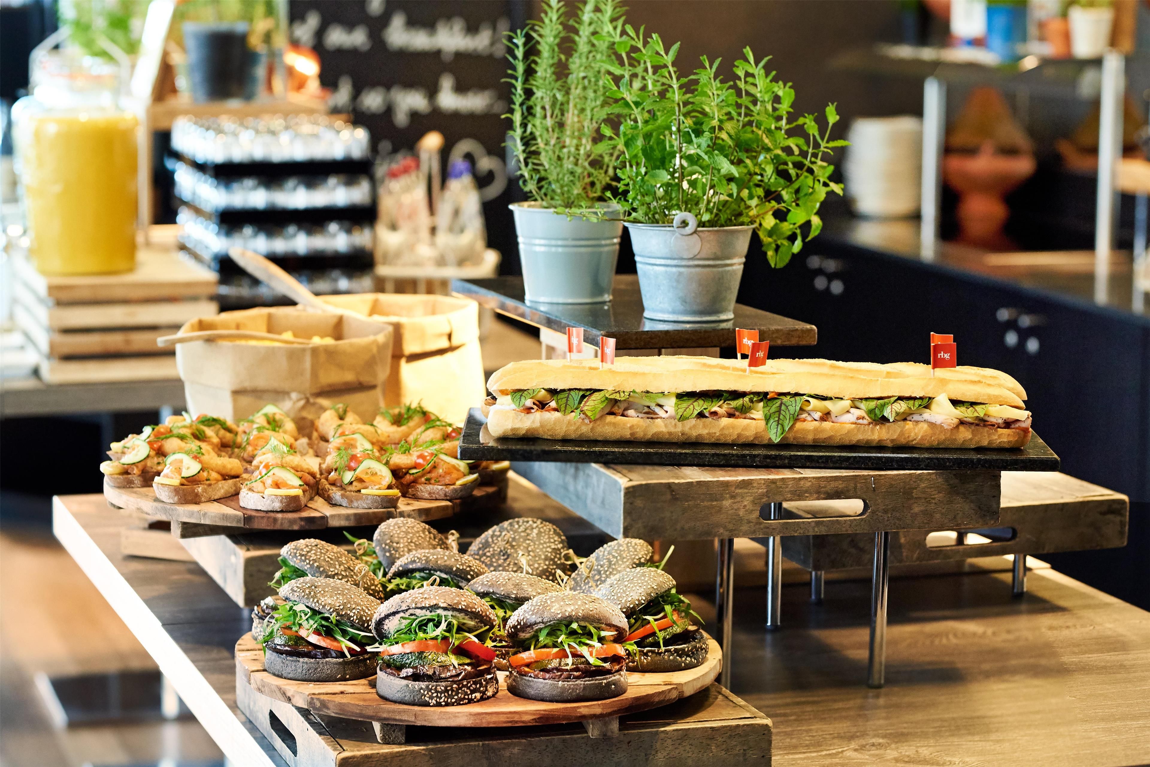 Diverse gerechten gepresenteerd op houten planken, waaronder sandwiches, burgers en kleine hapjes.
