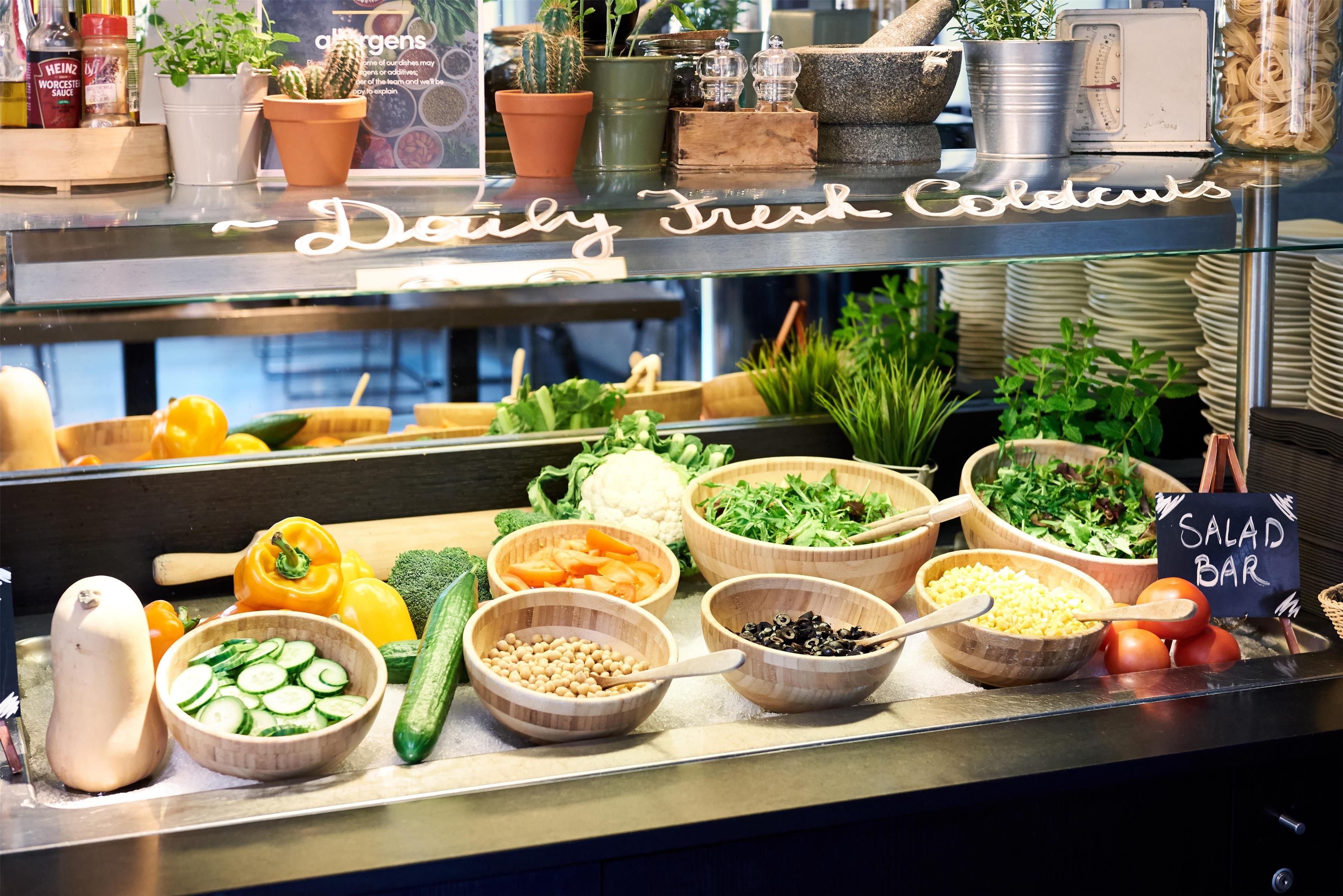 A salad bar with various fresh vegetables and a sign indicating it's a daily fresh salad bar.