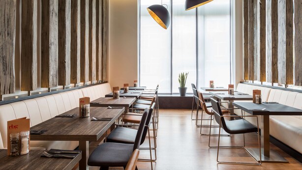 Un restaurant aux murs lambrés, doté de longues tables conviviales et éclairé par des suspensions noires.